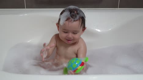 cheerful toddler happily playing with plastic toy while bathing in the bathtub