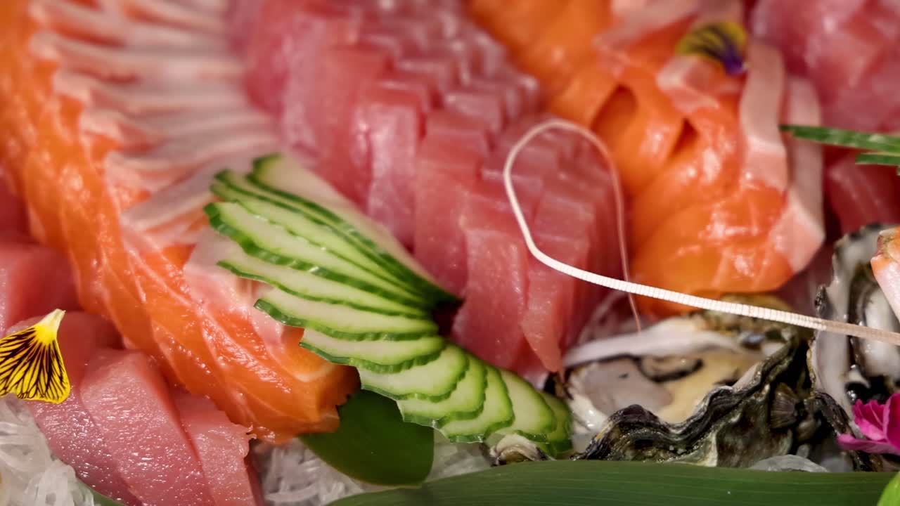 A detailed view of fresh salmon, tuna, and oysters garnished with cucumber and edible flowers.