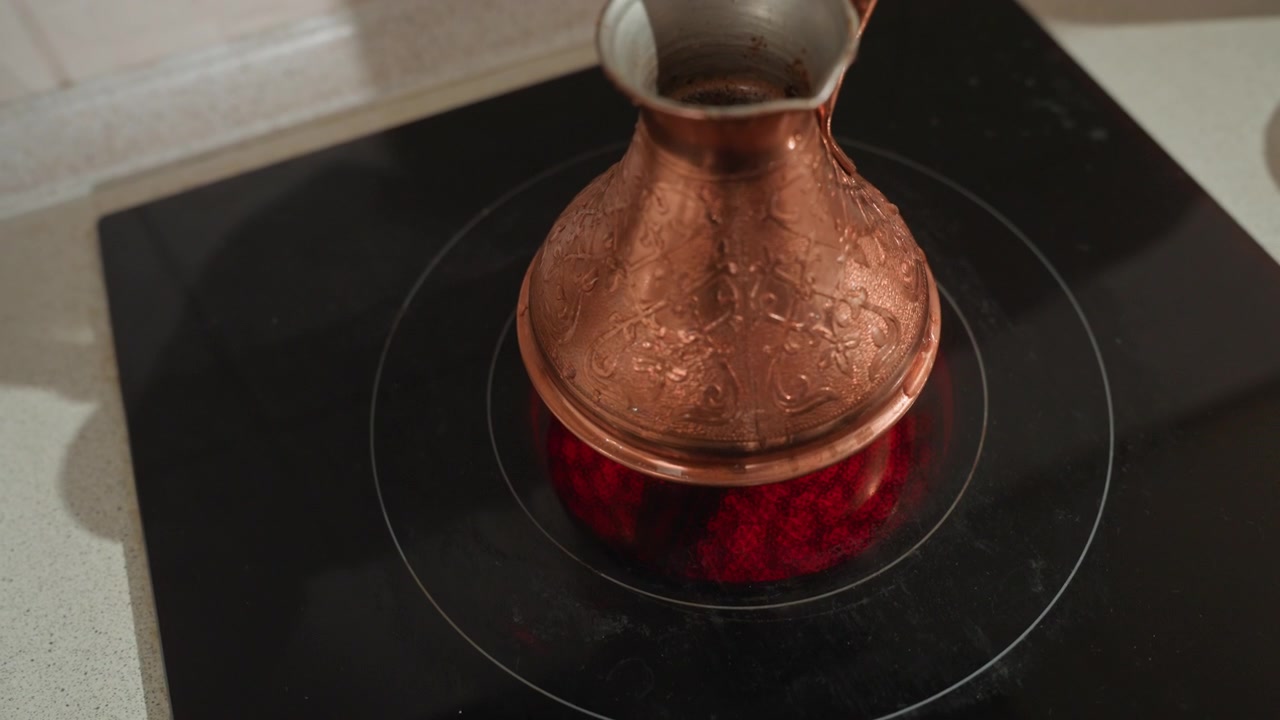 Copper cezve on stovetop heating coffee grounds simmering into thick crema, warm copper sheen, induction hob ring reflections, closeup texture, cozy morning ritual, slow living atmosphere