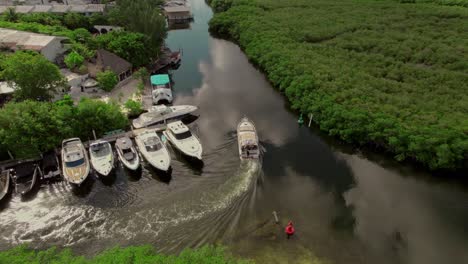 a motorboat passes a small harbor on a canal with dense greenery