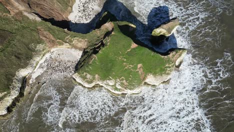overhead drone shot captures massive cliff towering over expansive seascape in england, uk. the rugged rock formation, contrasting beautifully with waves crashing it during daytime