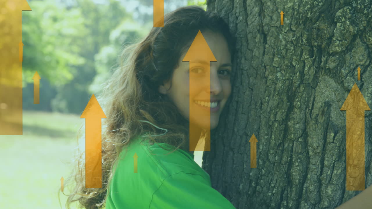 animación de flechas amarillas sobre una feliz mujer caucásica abrazando un árbol