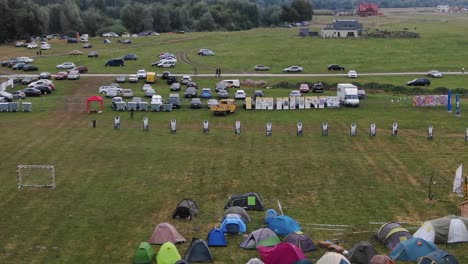 aerial view of multi-colored tents pitched in a field at a music festival with city in the background tracking forward