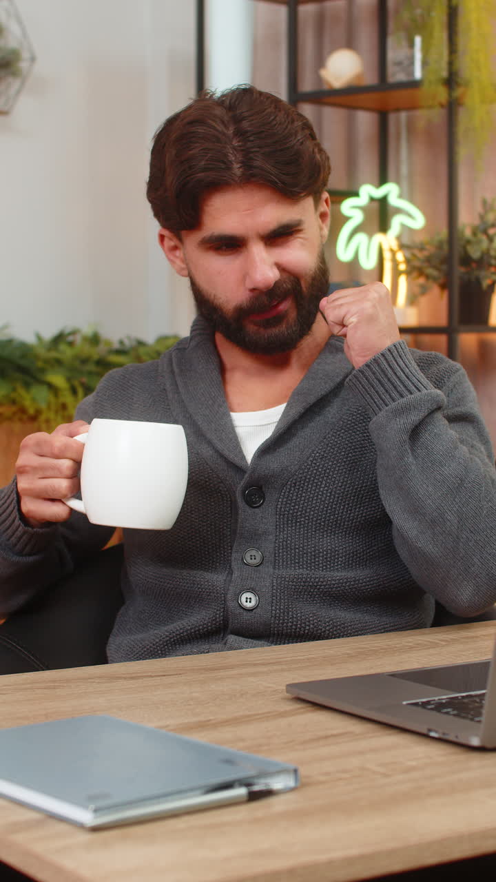 Indisk mand drikker kaffe eller te ved bærbar computer, tjekker to-do liste, markerer udført og giver tommel op, positiv glæde