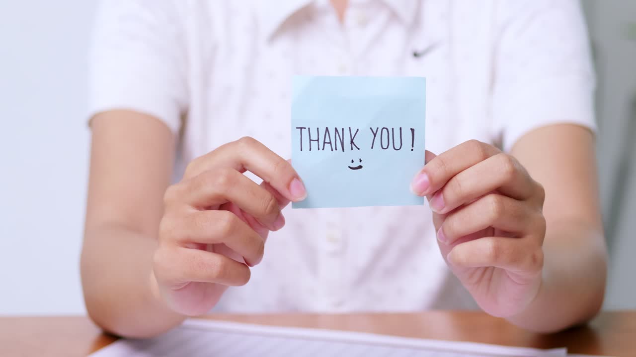 A close-up captures a person expressing gratitude with a handwritten thank you note