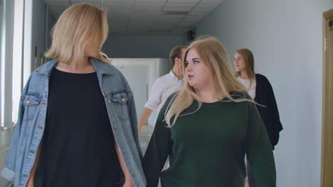 two female students walk down the hall of the university and talk and discuss and talk.