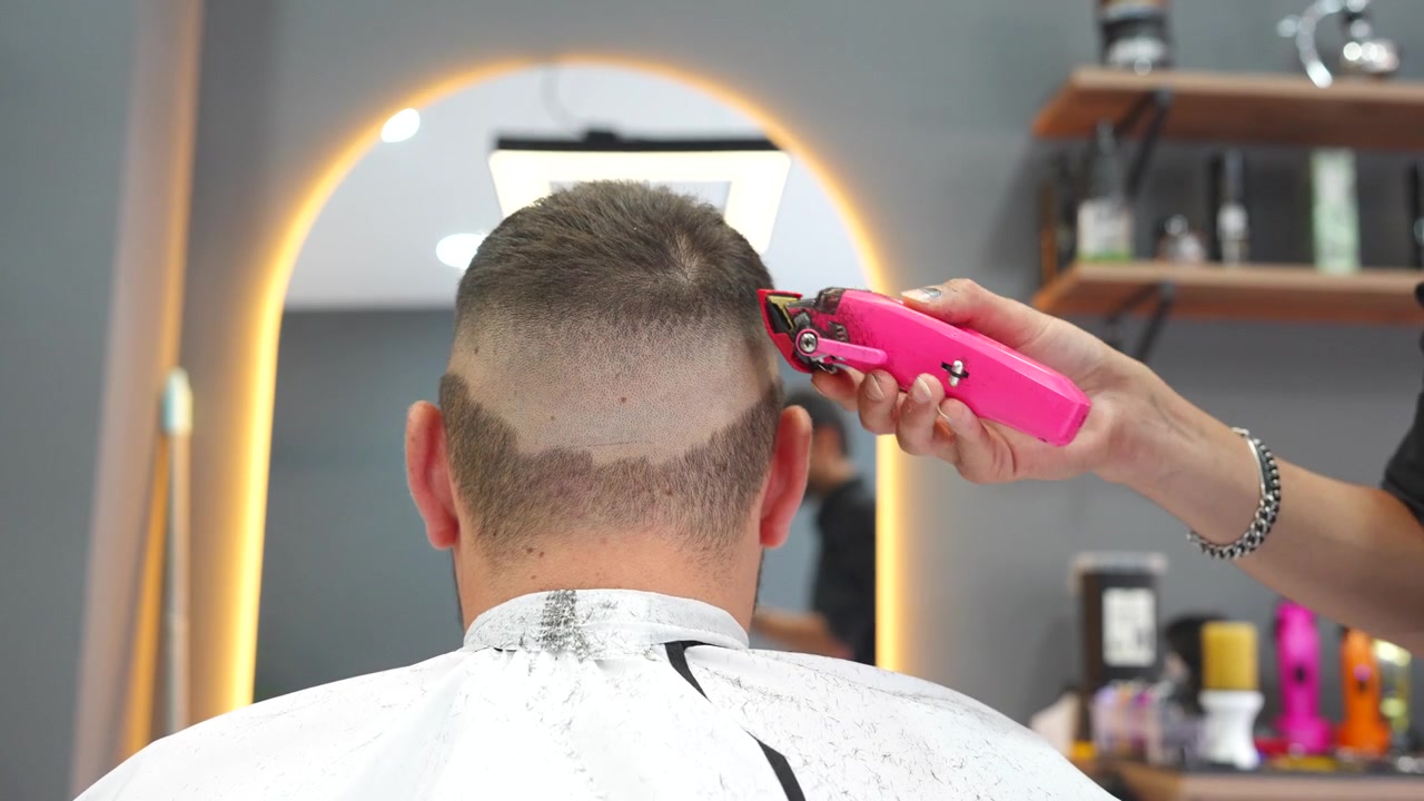 Professionel frisør skaber en fade-frisure til en mand med en elektrisk trimmer i en salon