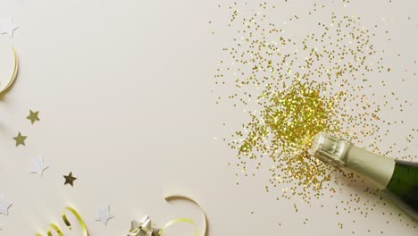 Video-of-champagne-bottle-with-gold-streamers,-stars,-glitter-and-baubles-on-white,-with-copy-space