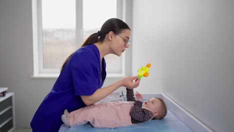 Glückliches-Brünettes-Mädchen-Mit-Brille-In-Blauer-Arztuniform-Spielt-Mit-Einem-Kleinen-Mädchen-Während-Eines-Termins-Mit-Kinderärzten-In-Einer-Modernen-Klinik