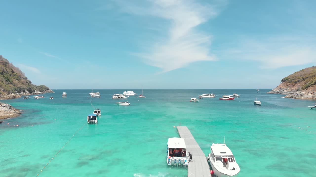 태국 푸켓 연안 코 라차 야이 섬의 관광 요트와 어선으로 붐비는 깨끗한 청록색 바다를 가로지르는 목조 부두 - 공중 비행 샷