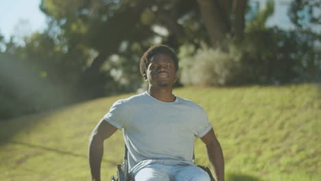 young black man riding his wheelchair in green summer park