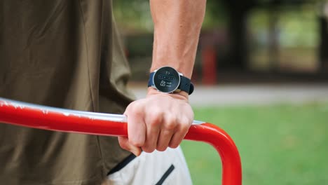 sporty man trains on machine in public park monitors his training session with smartwatch