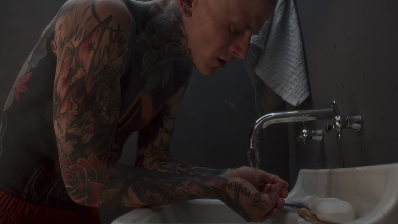 Homem Tatuado Sem Camisa Enxaguando o Rosto com Água na Pia da Cela da Prisão