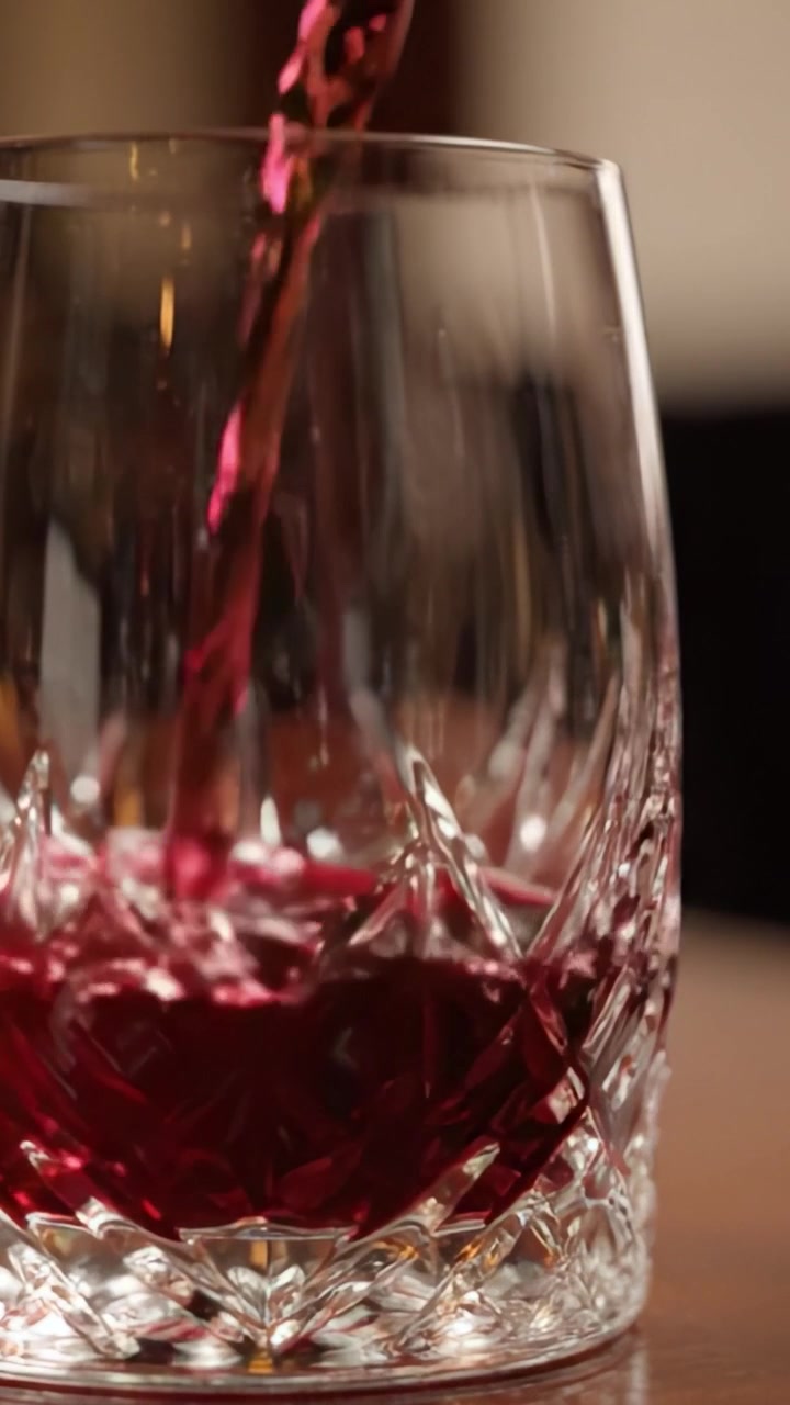 Un bicchiere di cristallo riempito con un ricco liquido rosso cattura la raffinatezza dei momenti di alta cucina in un ambiente di buon gusto