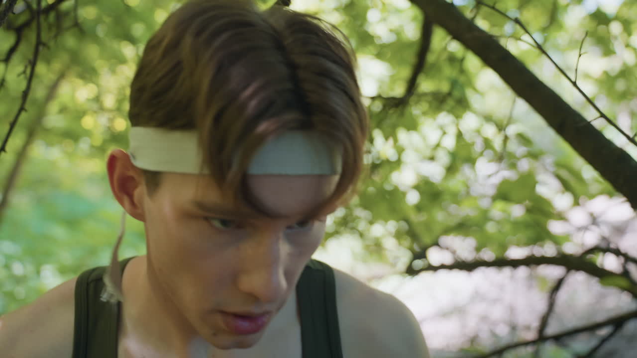 close up of tired tourist with brown hair covering forehead with gloved hand holding punch in forest combat training under dappled green foliage showing endurance and fierce determination