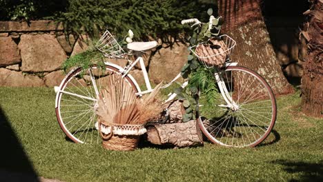 white vintage bicycle decorated with eucalyptus and wicker basket near stone wall and palm trees