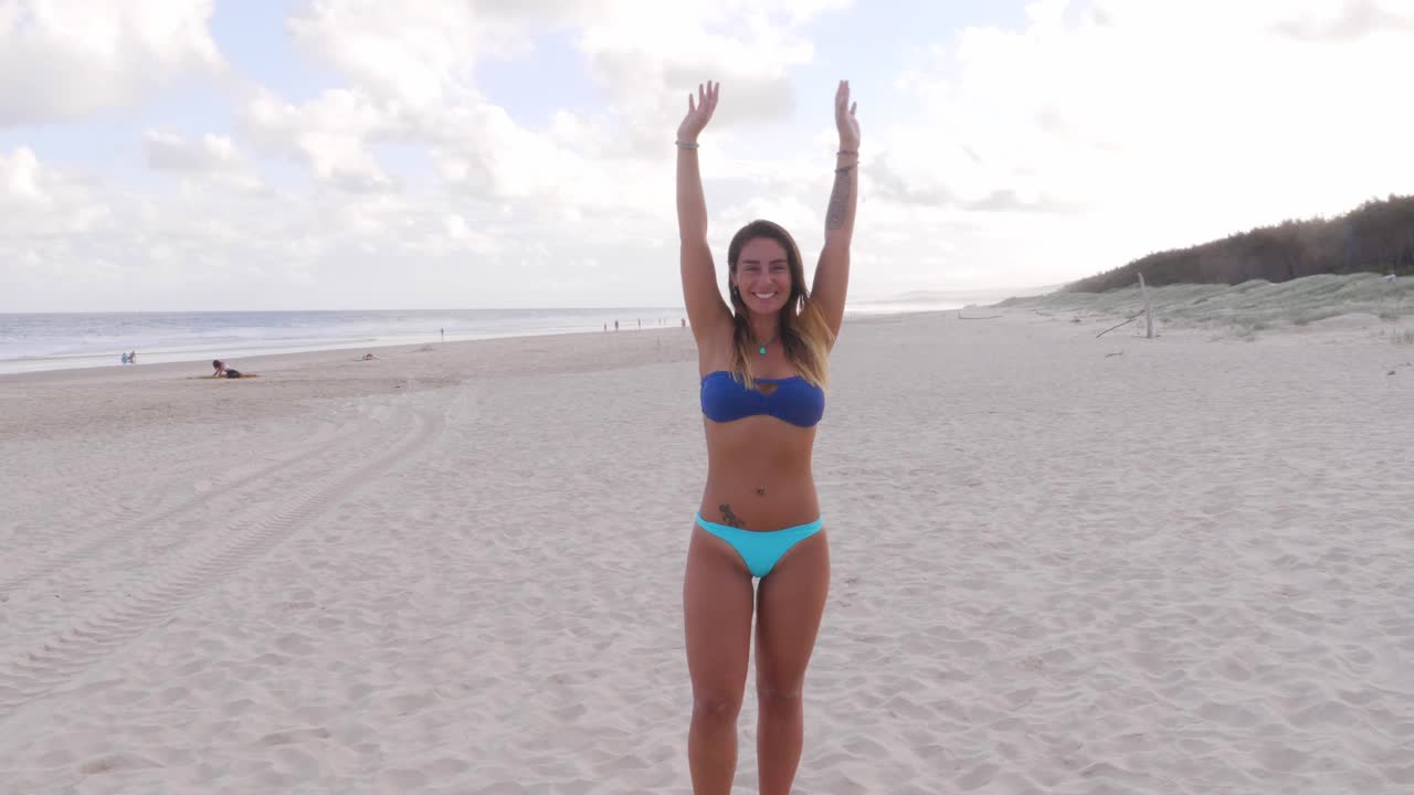 Ragazza sinuosa che alza le braccia in piedi sulla spiaggia principale a Point Lookout, Isola di North Stradbroke, QLD Australia