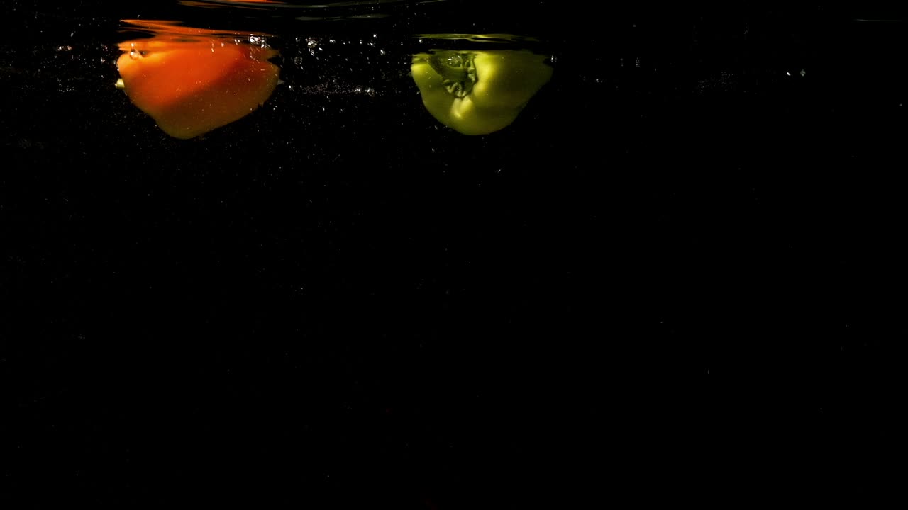 pimientos de pimienta naranja y verde flotando en el agua clara