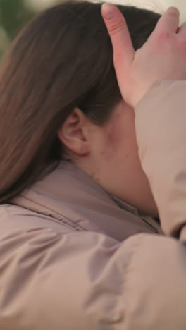 este primer plano captura a una mujer joven con una chaqueta de melocotón, caminando por un parque con una expresión reflexiva. su mano descansa en su frente, sugiriendo contemplación o tal vez fatiga