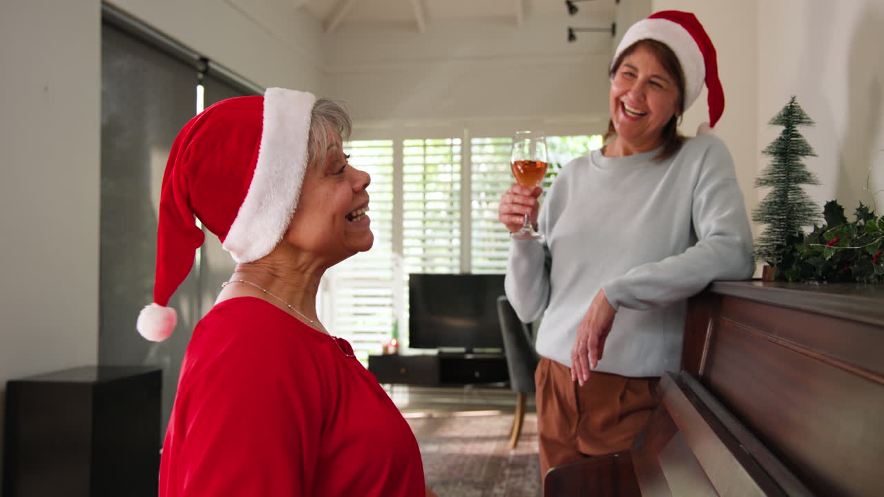 At Christmas, Senior women wearing Santa hats singing and laughing by piano at home