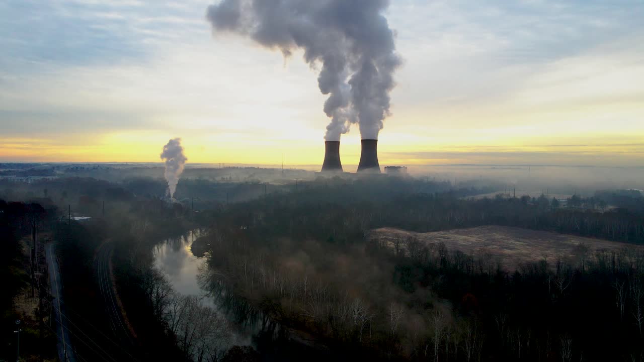 Un impianto nucleare all'alba, con le torri di raffreddamento che emettono vapore nel cielo dell'alba. Il movimento della telecamera è un lento sollevamento