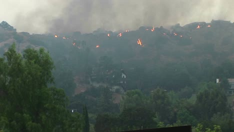 pan left shot of wildfires burning in the hills near a southern california community