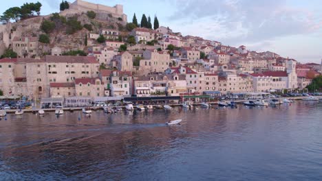 Boat-cruising-at-harbour-of-Sibenik-town-in-Croatia-during-sunset,-aerial