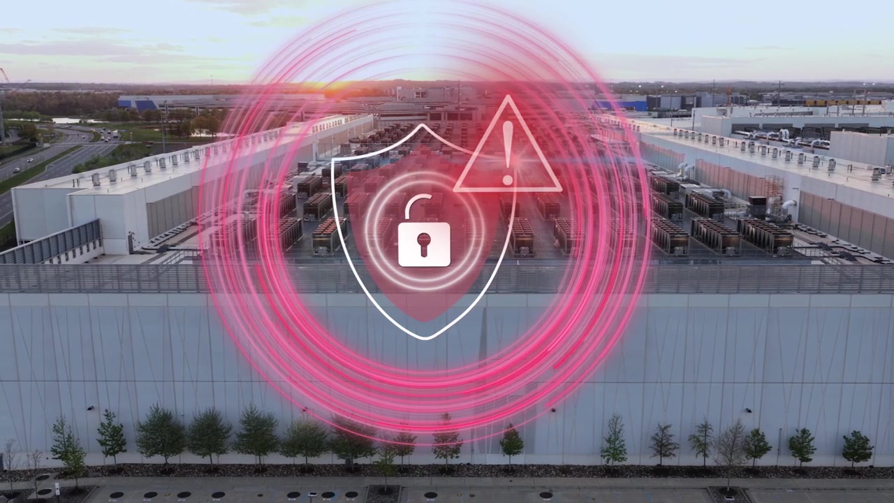 Struttura di data center con un'interfaccia digitale che mostra una violazione della sicurezza, caratterizzata da un'icona di avviso rossa e un lucchetto sbloccato che simboleggiano un attacco informatico o una fuga di dati. Vista aerea di data center americani.