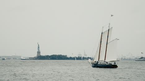 statue of liberty and liberty island in background as sail boat passes by the the new york harbor in new york city, new york, usa