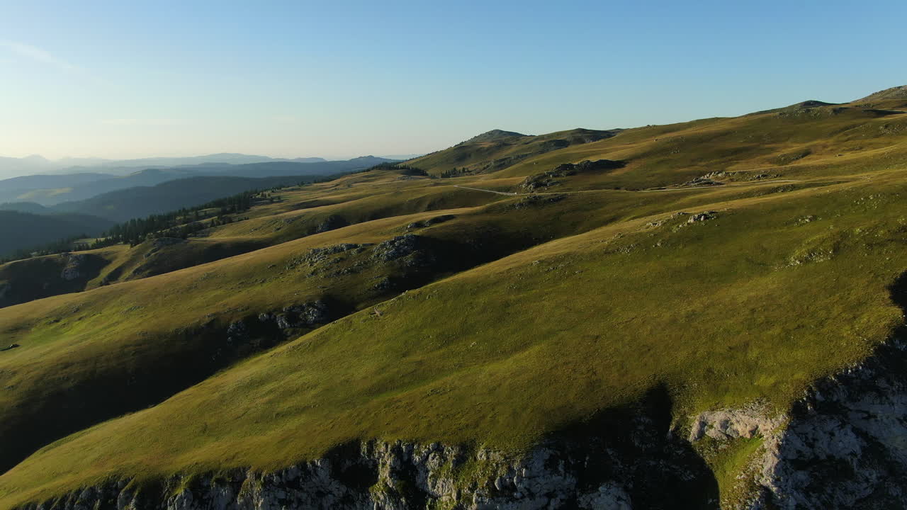 Hills covered in grass and rock formations Mountains in the distance under a clear sky Light and shadows on the landscape