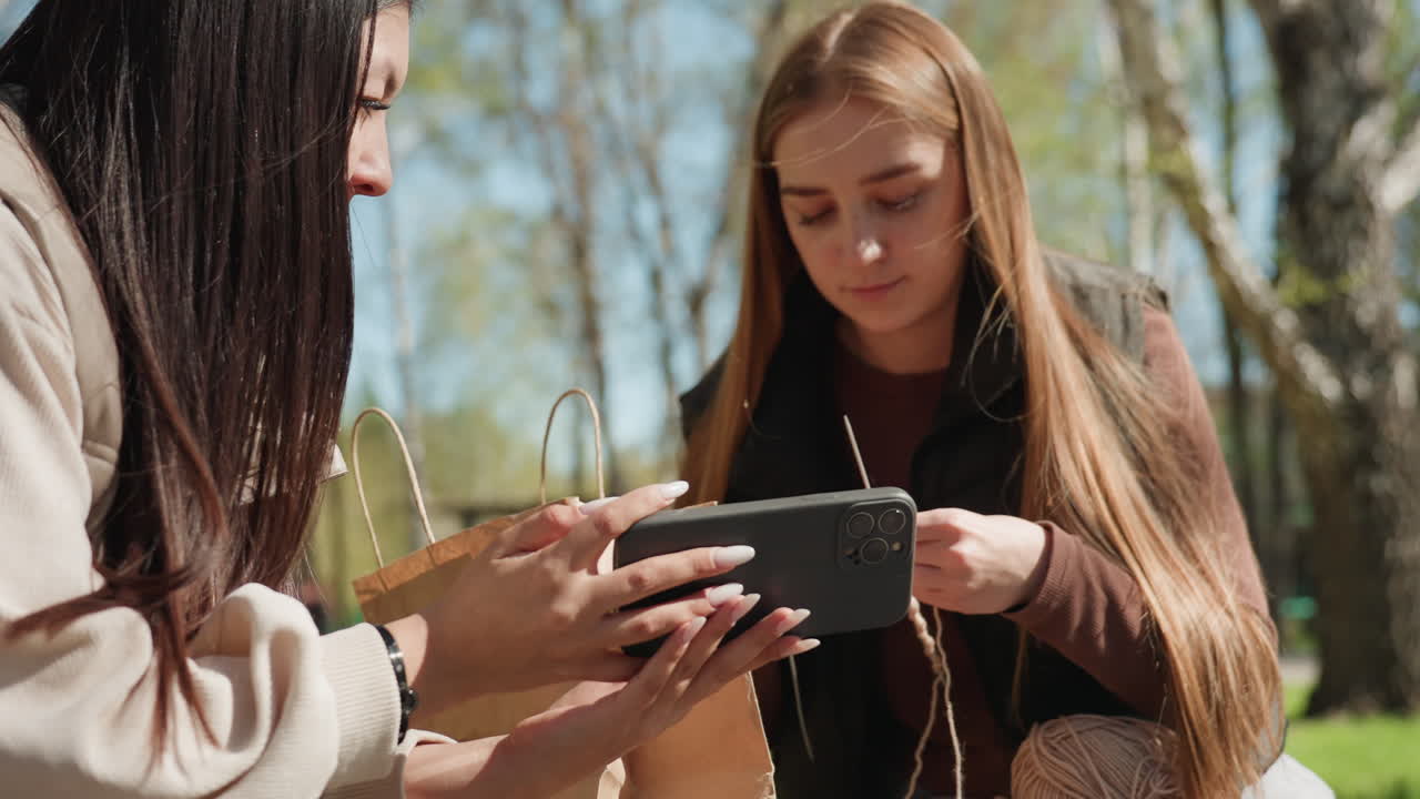 아시아인 멘토와 학생이 기기를 살펴보고 있어요. 멘토는 아시아인이고 학생은 휴대폰 사용에 집중하고 있어요. 아시아인 튜터와 백인 학생이 공원에서 함께 모바일 앱을 탐색하고 있습니다.