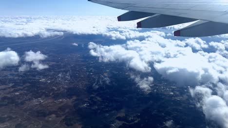 Vista-Aérea-Desde-La-Ventana-Del-Avión-Con-Vistas-A-Las-Nubes-Y-El-Paisaje,-La-Luz-Del-Día.