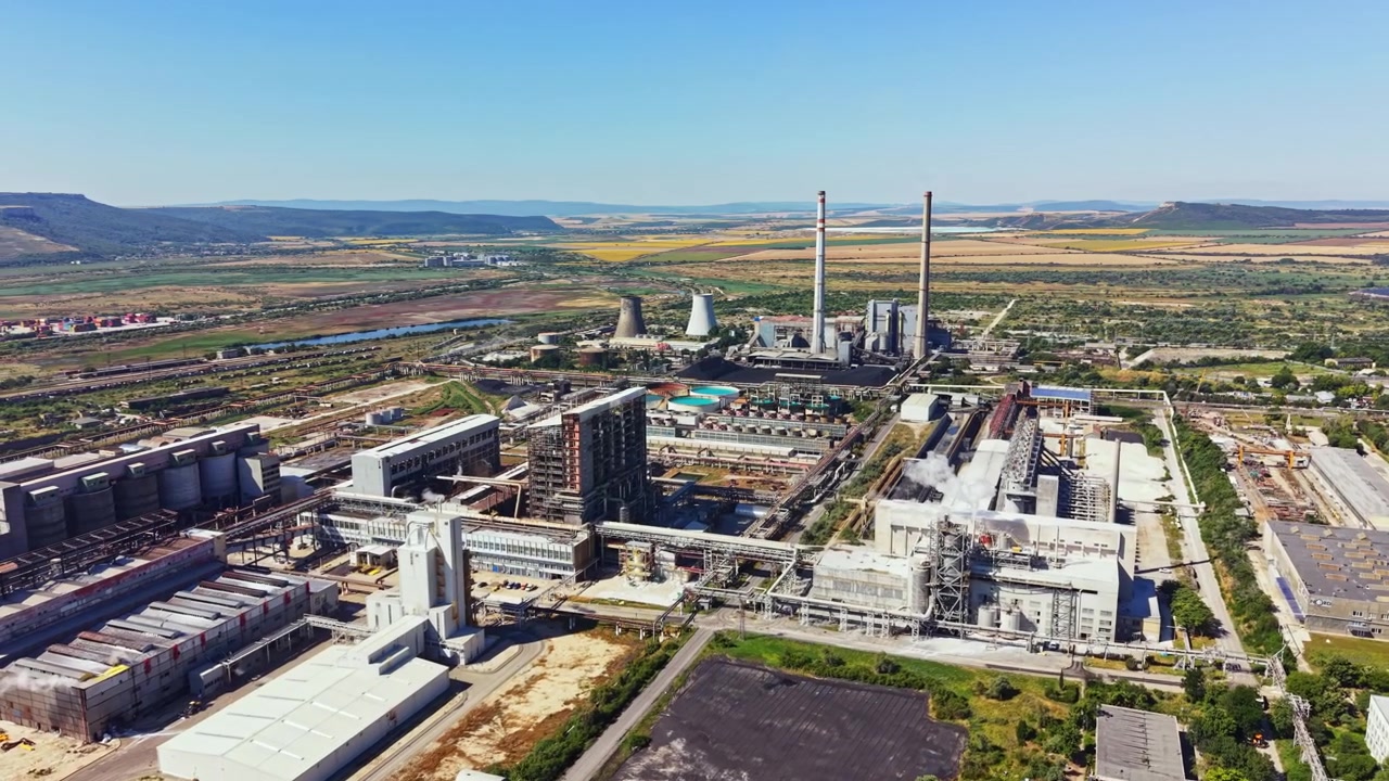 Sito industriale situato vicino a un fiume con edifici e alte ciminiere, di giorno e cielo azzurro limpido