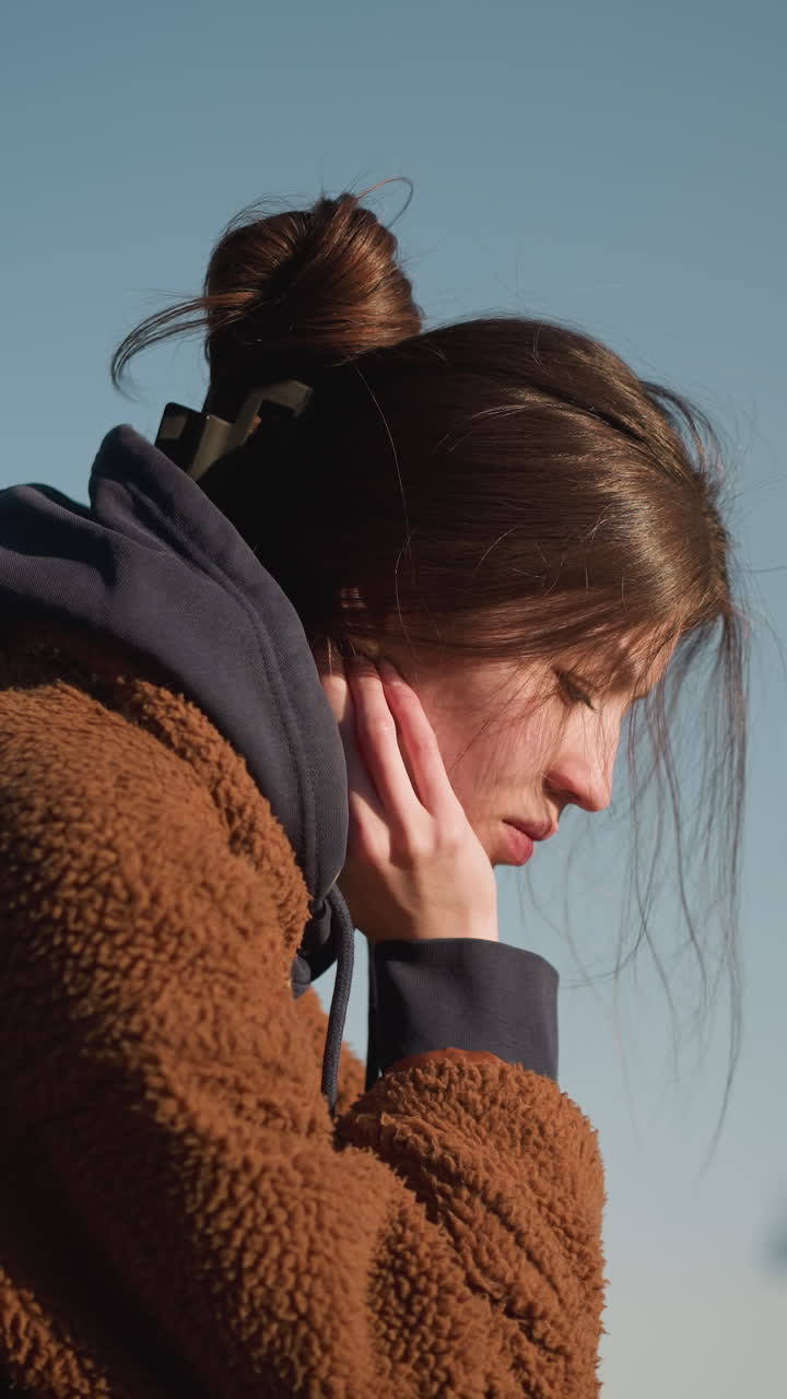 A close-up of a girl wearing a brown coat, looking deeply disturbed and lost in thought. emphasizing her emotional state. The background is a clear sky