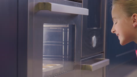 Close-Up-Of-Girl-Waiting-By-Oven-In-Kitchen-At-Home-For-Cakes-To-Bake