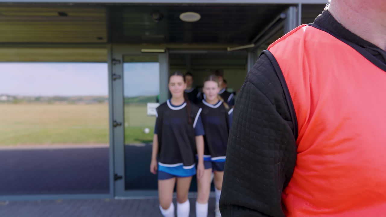Male and female soccer players wearing black vests entering pitch and running with coach