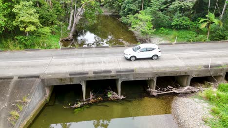 aerial footage of a car crossing a bridge over a creek in lush, dense jungle surroundings with vibrant greenery
