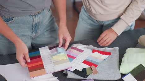 fabric designers selecting colors from vibrant color panel at creative studio while matching shades on work table filled with colorful textile swatches sewing supplies sketches