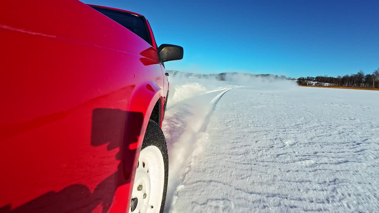 Actionbillede af rød pickupbil, der drifter på sneklædt mark på en solskinsdag.