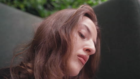 close up of light skin lady with blond hair looking downward in focused concentration, soft natural light highlighting her facial features, indoor setting with blurred greenery in background