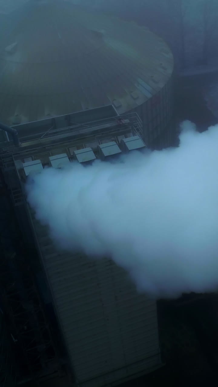 High premises on the territory of grain elevator plant with pipes producing thick smoke. Grey foggy day backdrop. Vertical video
