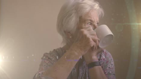 Animation-Von-Leuchtendem-Licht-über-Einer-Ernsthaften-älteren-Frau,-Die-Tee-Trinkt