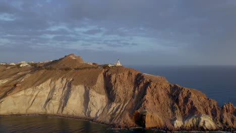 Aerial:-Approaching-Akrotiri-lighthouse-in-Santorini,-Greece-during-sunset