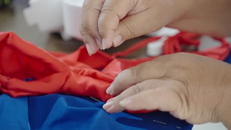 Tailor-stitches-red-and-blue-textile-together,-closeup-on-woman's-hands