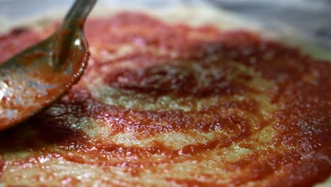 Metalllöffel,-Der-Eine-Tomatensauce-Auf-Einen-Pizzateig-Aufträgt,-Um-In-Zeitlupe-Eine-Pizza-Zuzubereiten