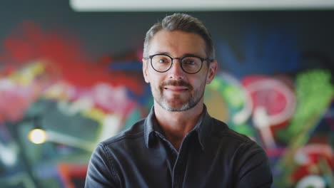 Middle-aged-white-male-creative-in-workplace-smiles-to-camera-and-crosses-arms,-head-and-shoulders