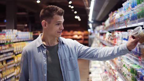 and attractive tall guy in supermarket. caucasian smiling young man in blue shirt choosing fresh milk from the fridge on store