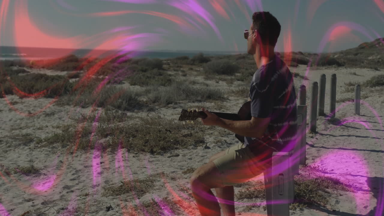 Man playing acoustic guitar on sandy beach dunes, showing swirling pink red music technology lights