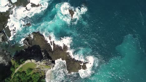 toma aérea de las olas del océano índico golpeando rocas y rocas en la playa en condiciones soleadas tiempo - pengilon hill, indonesia, asia