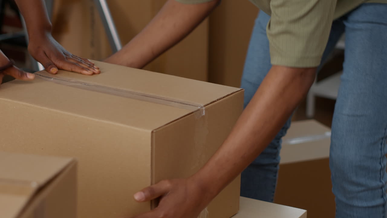 People wrapping up cardboard boxes with sticky tape roller